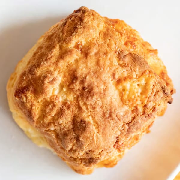Close-up of a golden-brown, freshly baked biscuit from Honest Biscuits on a white plate.
