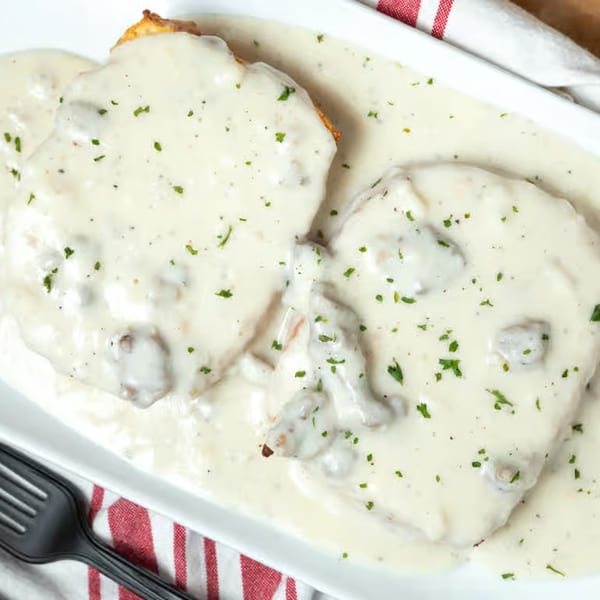 Two Honest Biscuits covered in creamy white gravy with chopped parsley, served on a white plate.
