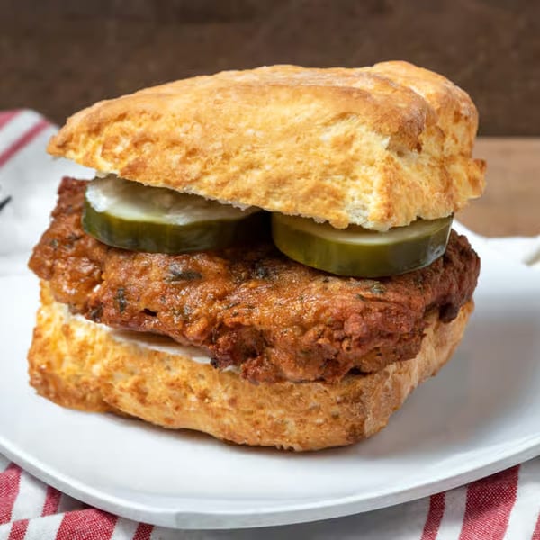 Honest Biscuits' fried chicken biscuit sandwich with pickles on a white plate with a red and white napkin.