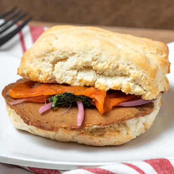 A breakfast biscuit sandwich with meat, roasted red peppers, spinach, and pickled onions.